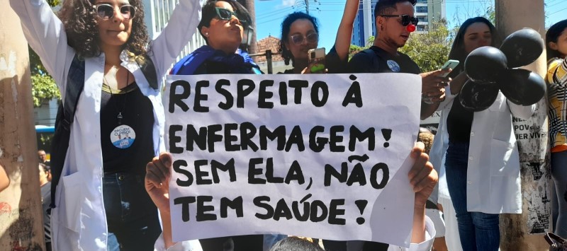Foto de ato da Enfermagem. Mulher segura cartaz, onde se lê: respeito à enfermagem! sem ela, não há saúde