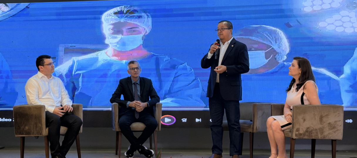 Quatro pessoas em um palco e um homem em pé falando ao microfone