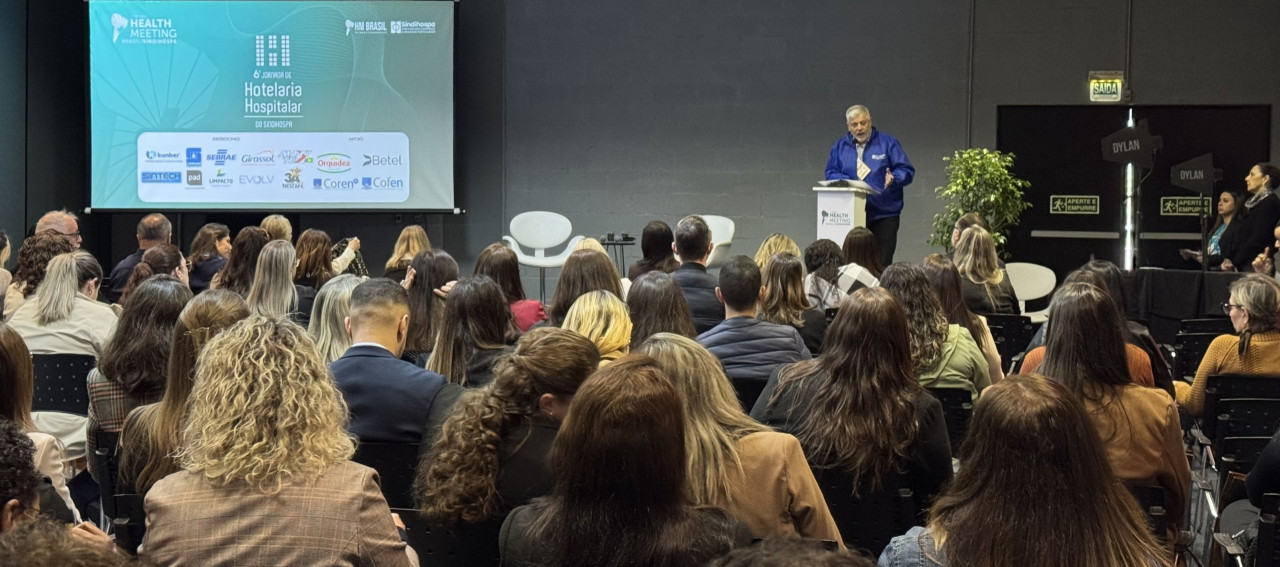 Uma pessoa falando ao microfone para pessoas sentadas em cadeiras