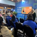 Uma mulher falando ao microfone para um público a sua frente