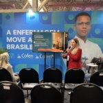 Uma pessoa falando ao microfone para pessoas sentadas em cadeiras