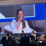Uma mulher falando ao microfone para um publico